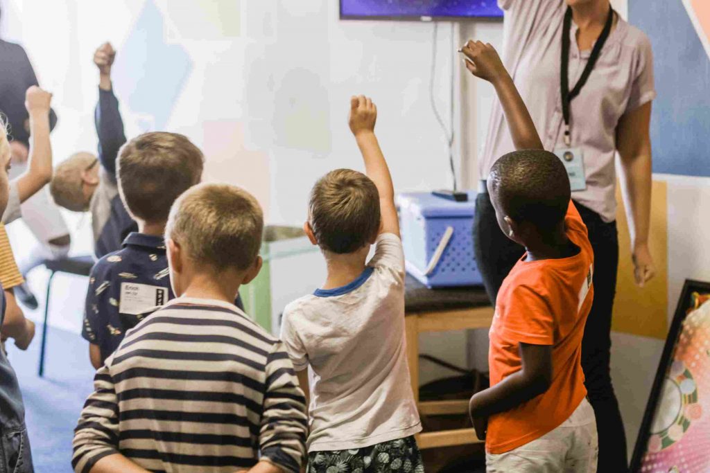 k-12 students raising their hands in class